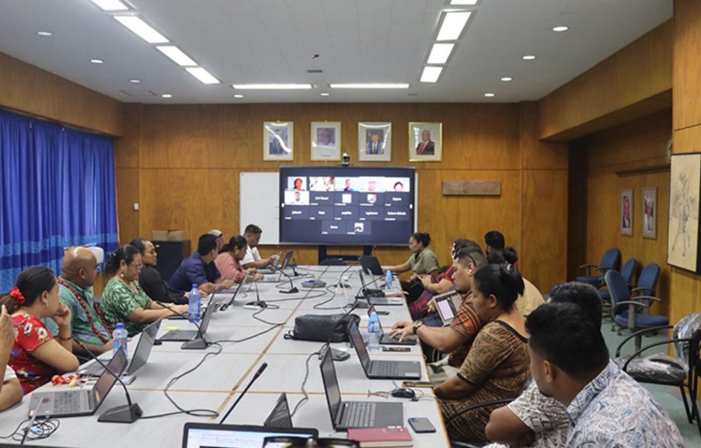 participants with laptops attending a Zoom presentation projected on boardroom screen